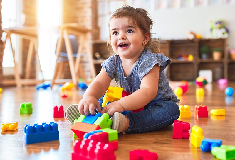 Beautiful toddler sitting on the floor playing with building blocks toys at kindergarten Beautiful toddler sitting on the floor playing with building blocks toys at kindergarten